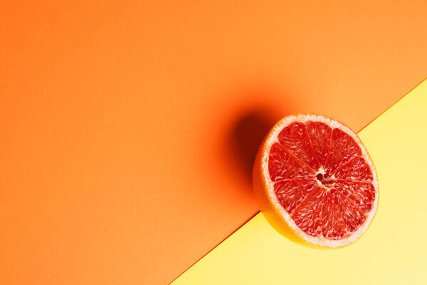 Close up of half of red grapefruit and copy space on orange and yellow background. Fruit, food, freshness and colour concept.
