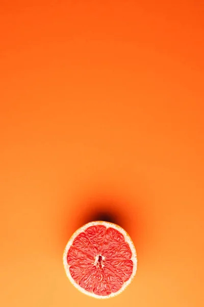 Close up of half of red grapefruit and copy space on orange background. Fruit, food, freshness and colour concept.