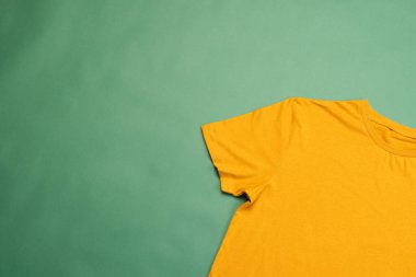 Turuncu tişört ve yeşil arka planda fotokopi alanı. Moda, kıyafetler, renk ve kumaş konsepti.