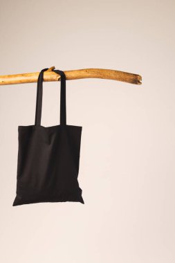 Ahşap dalda asılı siyah bez çanta ve beyaz arka planda fotokopi alanı. Alışveriş, çanta, renk, kumaş, doku ve malzeme kavramı.