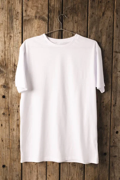 White t shirt on hanger and copy space on wooden background. Fashion, clothes, colour and fabric concept.