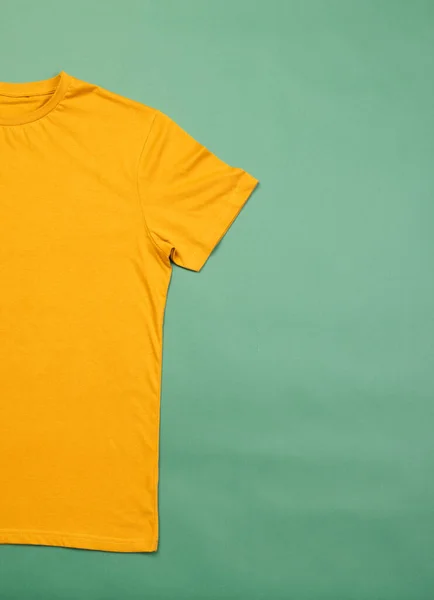 Orange t shirt and copy space on green background. Fashion, clothes, colour and fabric concept.
