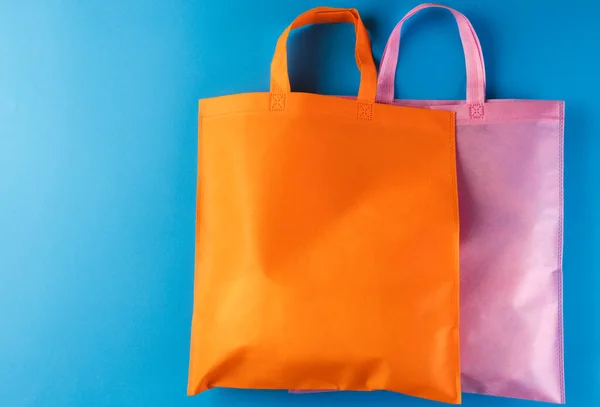 青い背景のコピースペースが付いているオレンジおよびピンクのキャンバス袋 ショッピング バッグ カラー ファブリック テクスチャ 素材コンセプト — ストック写真