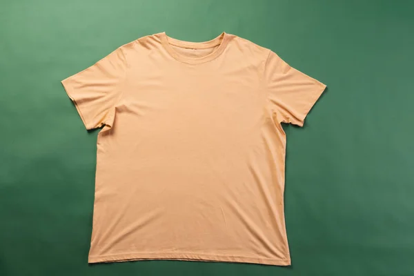 Orange t shirt and copy space on green background. Fashion, clothes, colour and fabric concept.