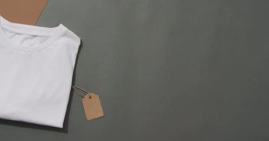 Gri ve kahverengi arkaplan üzerinde etiket ve kopyalama alanı olan katlanmış beyaz tişört yatağı videosu. Giysi, kumaş, doku ve malzeme konsepti.