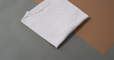 Gri ve kahverengi arkaplanda fotokopi alanı olan katlanmış beyaz t-shirt 'ün olduğu bir video. Giysi, kumaş, doku ve malzeme konsepti.