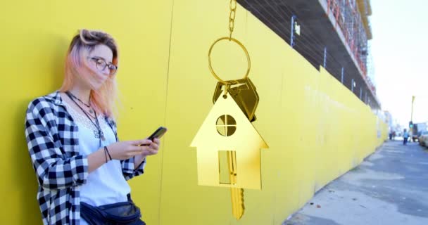 通りのスマートフォンを使用して白人女性の上に金の家の鍵を吊るすアニメーション 不動産技術コンセプト — ストック動画