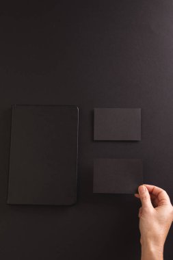 Siyah defter ve siyah arka planda siyah kağıt tutan beyaz kadının dikey görüntüsü. Kağıt, yazı, doku ve malzeme kavramı.