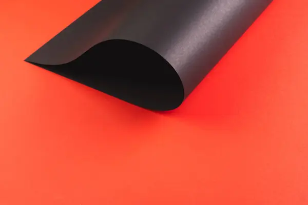 赤い背景のコピースペースで巻き上げられた黒いペーパーのクローズアップ ライティング テクスチャ 素材コンセプト — ストック写真