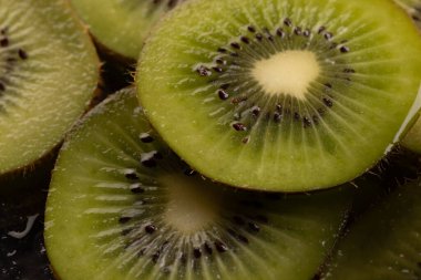 Dilimlenmiş kivi meyvelerini su damlalarıyla mikro yakından çek ve siyah arkaplanda boşluğu kopyala. Mikro fotoğrafçılık, yemek, doku ve renk kavramı.