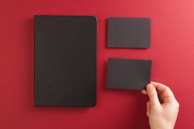 Siyah defter ve kırmızı arka planda siyah kağıt tutan beyaz kadın. Kağıt, yazı, doku ve malzeme kavramı.