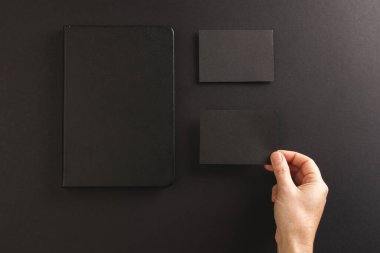 Siyah defter ve siyah arka planda siyah kağıt tutan beyaz kadın. Kağıt, yazı, doku ve malzeme kavramı.