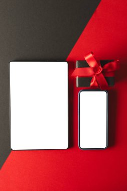 Tablet ve akıllı telefonun dikey görüntüsü boş ekran ve kırmızı ve siyah arkaplan üzerinde hediye. Siber Pazartesi, siber alışveriş, perakende, teknoloji, elektronik cihaz ve iletişim konsepti.