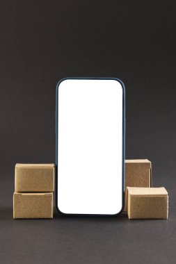 Boş ekran ve karton kutuları olan akıllı telefonun dikey görüntüsü, siyah arkaplana boşluğu kopyala. Siber Pazartesi, siber alışveriş, perakende, teknoloji, elektronik cihaz ve iletişim konsepti.