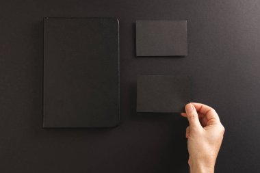 Siyah defter ve siyah arka planda siyah kağıt tutan beyaz kadın. Kağıt, yazı, doku ve malzeme kavramı.