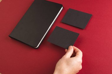 Siyah defter ve kırmızı arka planda siyah kağıt tutan beyaz kadın. Kağıt, yazı, doku ve malzeme kavramı.