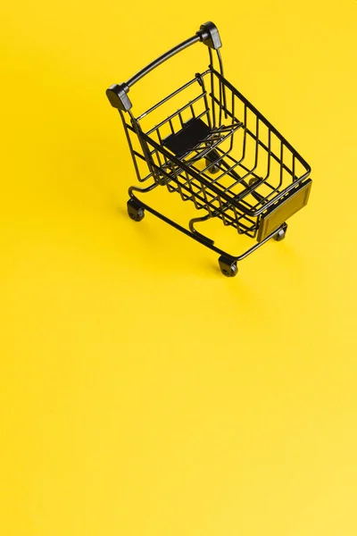 黄色の背景にコピースペースを持つ黒いショッピングトロリーの垂直画像 サイバー月曜日 サイバーショッピング テクノロジー 電子デバイス 通信コンセプト — ストック写真