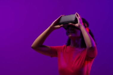 Çift ırklı kadın, neon pembeden mor arka plana vr kulaklık kullanıyor. Teknoloji, dijital ağlar, küresel bağlantılar ve iletişim metaevreleri.