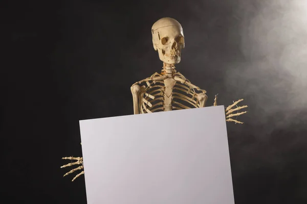 Plastic Skeleton Holding Paper Sheet Smoke Copy Space Black Background — Stock Photo, Image
