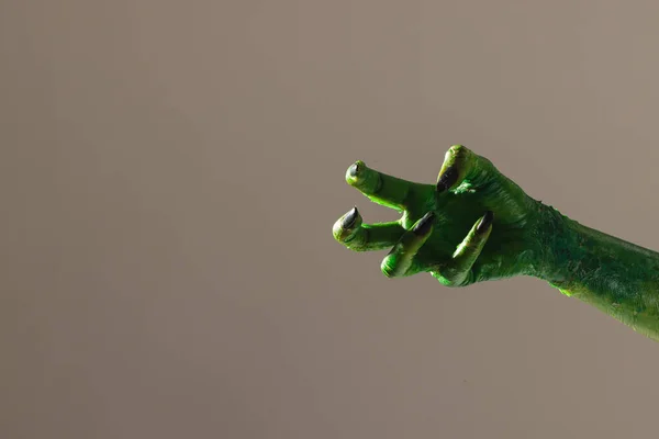 Green monster hand with black nails making gesture on grey background. Halloween, tradition and celebration concept.