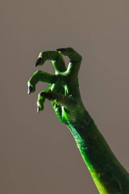 Siyah tırnaklı yeşil canavar elin dikey görüntüsü gri arka planda jest yapıyor. Cadılar Bayramı, gelenek ve kutlama konsepti.