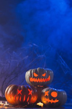 Mavi zemin üzerinde kopya alanı olan üç kabak ve mumların dikey görüntüsü. Sonbahar, sonbahar, cadılar bayramı, gelenek ve kutlama konsepti.