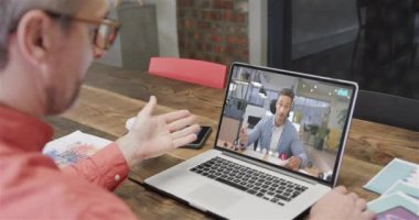 Kafkasyalı iş adamı, ekranda beyaz bir erkek arkadaşla görüntülü konuşma yapıyor. Çevrimiçi bağlantılar, iş ve ağ oluşturma kavramı.