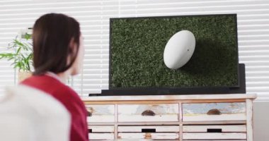 Beyaz kadın, stadyumda ragbi topuyla televizyon izliyor. İletişim teknolojisi ve spor, dijital kompozit video.