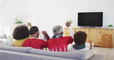 Çift ırklı aile, stadyumdaki ragbi topuyla televizyon izliyor. İletişim teknolojisi ve spor, dijital kompozit video.