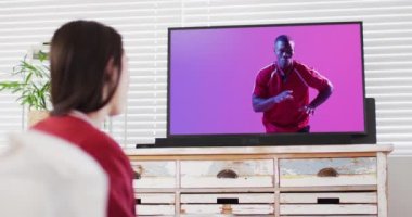 Beyaz kadın, Afrika asıllı Amerikalı erkek rugby oyuncusuyla televizyon izliyor. İletişim teknolojisi ve spor, dijital kompozit video.