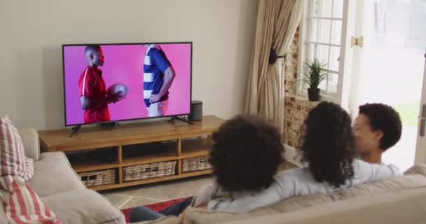 Zweirassige Familie Vor Dem Fernseher Mit Verschiedenen Männlichen Rugby Spielern — Stockvideo