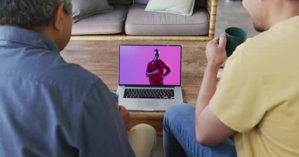 ボールを持ったアフリカ系アメリカ人男性ラグビー選手とラップトップを見ているBiracialの父と息子 コミュニケーション技術とスポーツ デジタル複合ビデオ — ストック動画