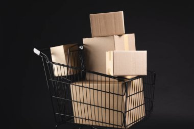 Kutularla dolu bir alışveriş arabası ve siyah arka planda fotokopi alanı. Siber Pazartesi, Kara Cuma, çevrimiçi alışveriş, nakliye ve küresel bağlantılar kavramı.