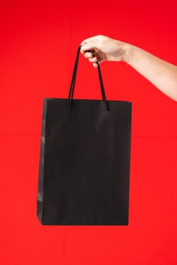 Elinde kırmızı arka planda fotokopi alanı olan siyah hediye çantası tutan beyaz bir kadın. Kara Cuma, siber pazartesi, alışveriş, siber alışveriş, satış, perakende ve nakliye konsepti.