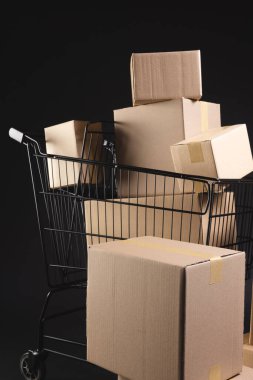 Kutuları olan alışveriş arabasının dikey görüntüsü ve siyah arkaplan üzerine kopyalama alanı. Siber Pazartesi, Kara Cuma, çevrimiçi alışveriş, nakliye ve küresel bağlantılar kavramı.