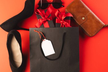 Hediye çantası, hediye kutuları, ayakkabılar, cüzdan, güneş gözlükleri ve kırmızı arkaplanda fotokopi alanı. Siber Pazartesi, Kara Cuma, çevrimiçi alışveriş, nakliye ve küresel bağlantılar kavramı.
