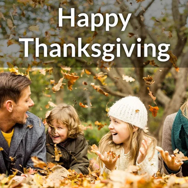 Happy thanksgiving text over happy caucasian parents and children playing in autumn leaves. Thanksgiving, harvest festival, american tradition, family and autumn celebration digitally generated image.