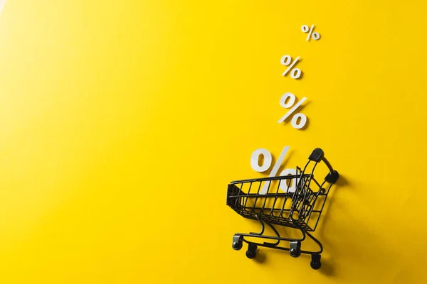 Shopping trolley and white percent signs with copy space on yellow background. Black friday, cyber monday, shopping, cyber shopping, sales, retail and shipping concept.
