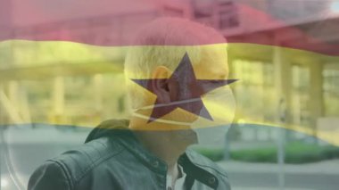 Caddede yüzü maskeli beyaz bir adamın portresinin üzerinde sallanan Gana bayrağının animasyonu. Küresel covid-19 salgın konsepti
