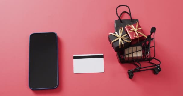 白い画面 クレジット カード 赤い背景のショッピング トロリーが付いているスマートフォンのビデオ サイバーショッピング オンライン配送 テクノロジー グローバルコネクションのコンセプト — ストック動画