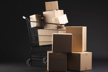 Kutularla dolu bir alışveriş arabası ve siyah arka planda fotokopi alanı. Siber Pazartesi, Kara Cuma, çevrimiçi alışveriş, nakliye ve küresel bağlantılar kavramı.