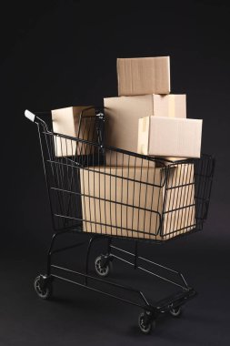 Kutuları olan alışveriş arabasının dikey görüntüsü ve siyah arkaplan üzerine kopyalama alanı. Siber Pazartesi, Kara Cuma, çevrimiçi alışveriş, nakliye ve küresel bağlantılar kavramı.