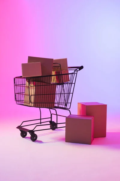 Kutuları Olan Alışveriş Arabasının Dikey Görüntüsü Neon Mor Arkaplan Üzerine — Stok fotoğraf