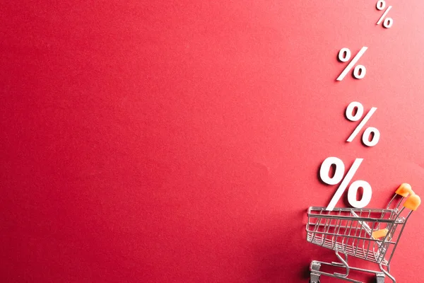 Shopping trolley and white percent signs with copy space on red background. Black friday, cyber monday, shopping, cyber shopping, sales, retail and shipping concept.