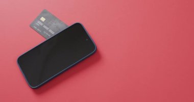 Akıllı telefonun boş ekranlı videosu, kutular ve kırmızı arka planda fotokopi alanı olan kredi kartı. Siber alışveriş, çevrimiçi taşımacılık, teknoloji ve küresel bağlantılar kavramı.