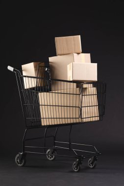 Kutuları olan alışveriş arabasının dikey görüntüsü ve siyah arkaplan üzerine kopyalama alanı. Siber Pazartesi, Kara Cuma, çevrimiçi alışveriş, nakliye ve küresel bağlantılar kavramı.