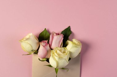 Kahverengi zarf içinde beyaz ve pembe gül çiçekleri ve pembe arka planda kopyalama alanı. Çiçek, bitki, şekil, doğa ve renk kavramı.