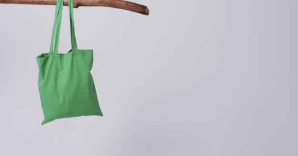 白い背景のコピースペースで枝からぶら下がっている緑のキャンバスバッグのビデオ バッグ ショッピング ファッション ファブリックのコンセプト — ストック動画