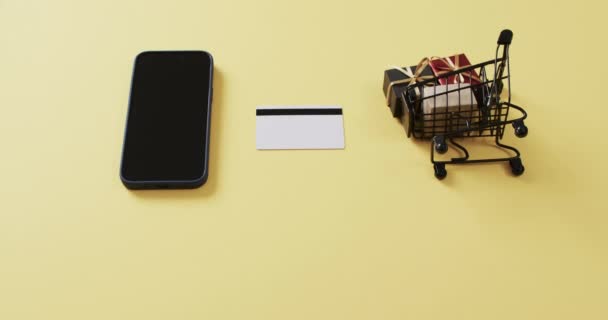 白い画面 クレジット カード 黄色の背景のショッピング トロリーが付いているスマートフォンのビデオ サイバーショッピング オンライン配送 テクノロジー グローバルコネクションのコンセプト — ストック動画