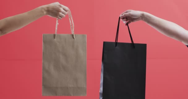 赤い背景にコピースペースを持つショッピングバッグを持っている白人女性の手のビデオ ブラックフライデー サイバー月曜日 ショッピング サイバーショッピング セールス 出荷コンセプト — ストック動画